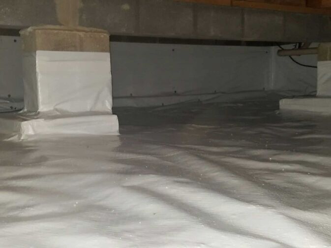 A crawl space with concrete support pillars, covered in a clean, white vapor barrier liner for moisture control.