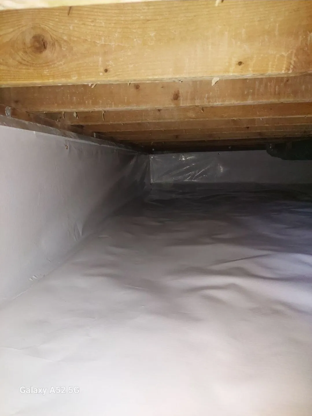 A crawl space with a plastic vapor barrier installed on the floor and walls, and wooden floor joists visible above.