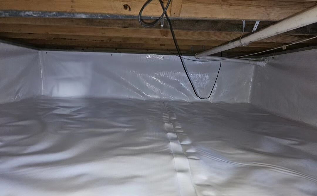 A crawl space with a plastic vapor barrier installed on the floor and lower walls, exposed wooden beams above, a hanging cable, and a white PVC pipe running along the ceiling.