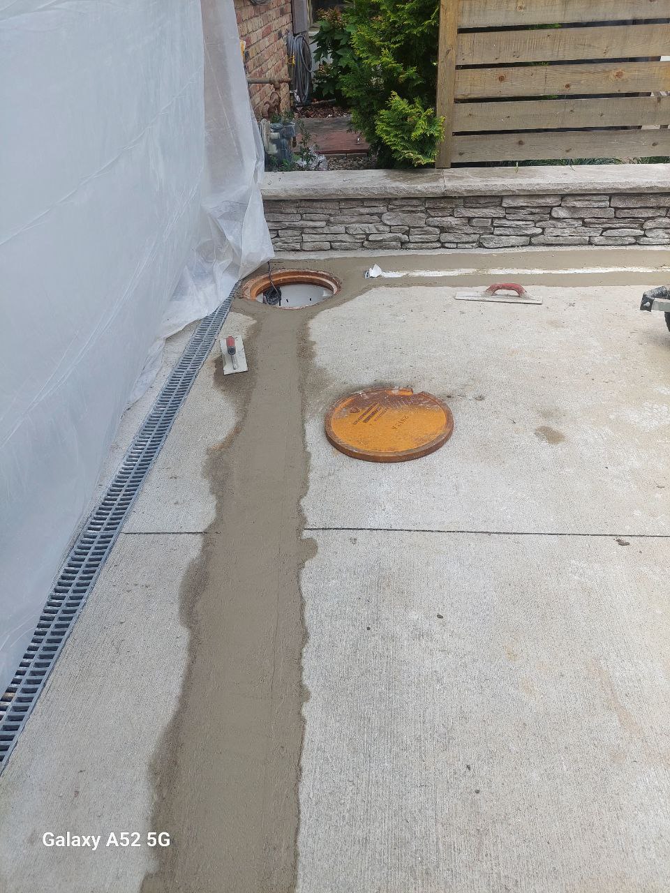 A freshly patched concrete surface with visible repair lines, two circular access covers, and drainage grates along the edge.