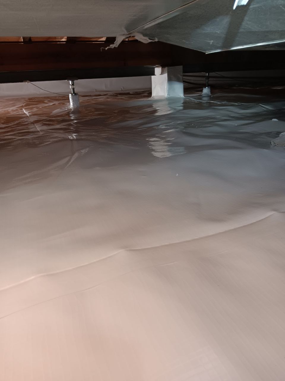 A crawlspace with a clean, sealed vapor barrier covering the floor and support beams visible in the background.
