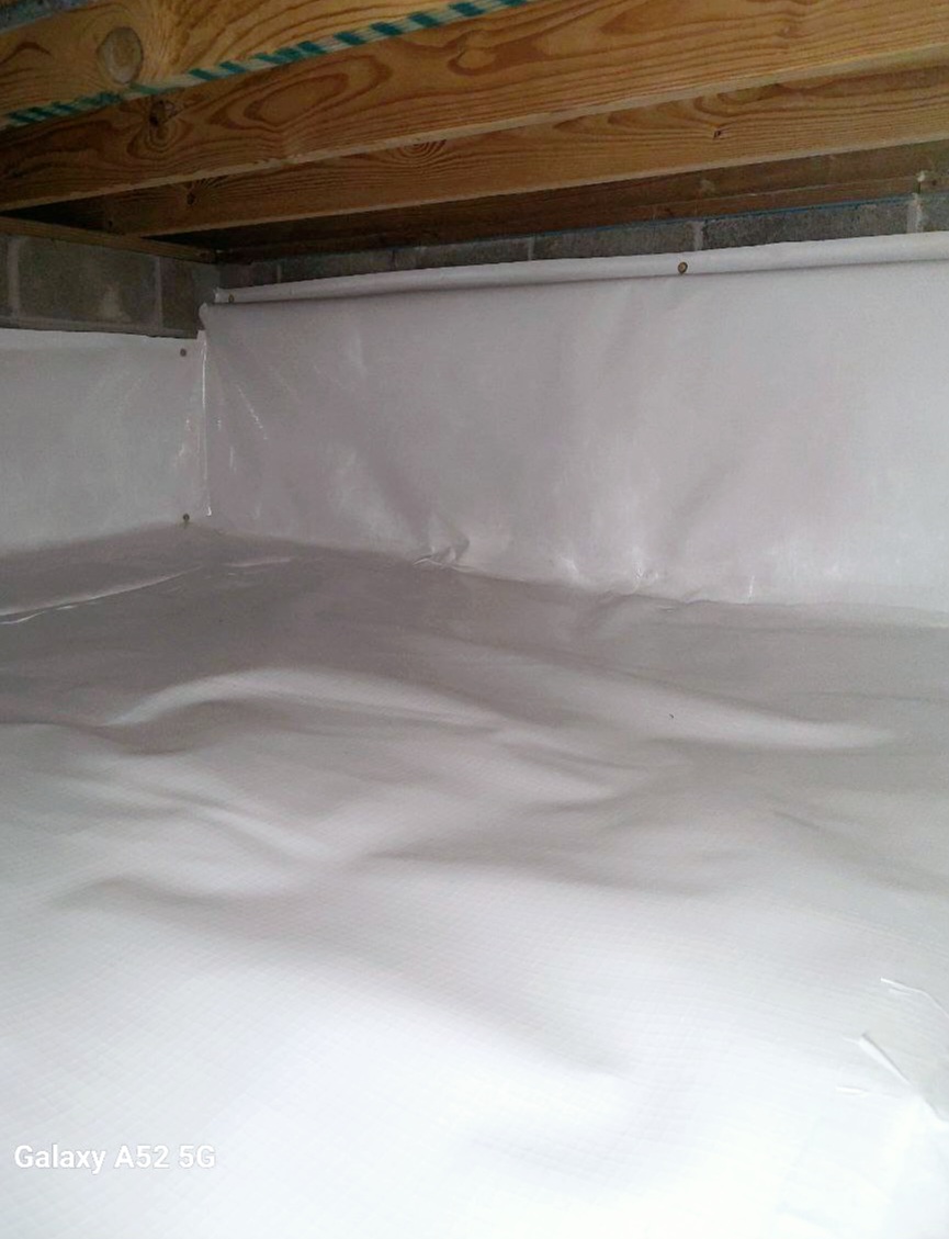 A crawl space with a plastic vapor barrier installed on the floor and walls, exposed wooden joists above, and concrete blocks along the side.