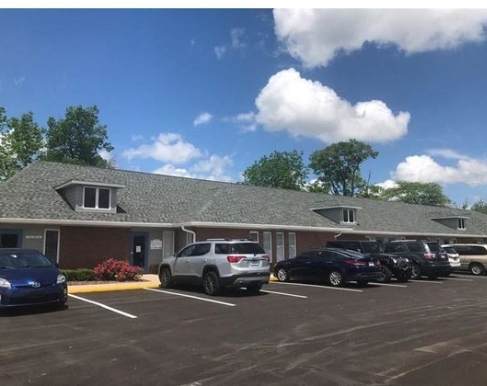 Single-story brick office building with a gray roof, several parked cars in front, and a blue sky with scattered clouds overhead.
