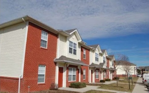Row of two-story townhouses with red brick and light siding exteriors, under a partly cloudy blue sky, with sidewalks and small bushes in front.
