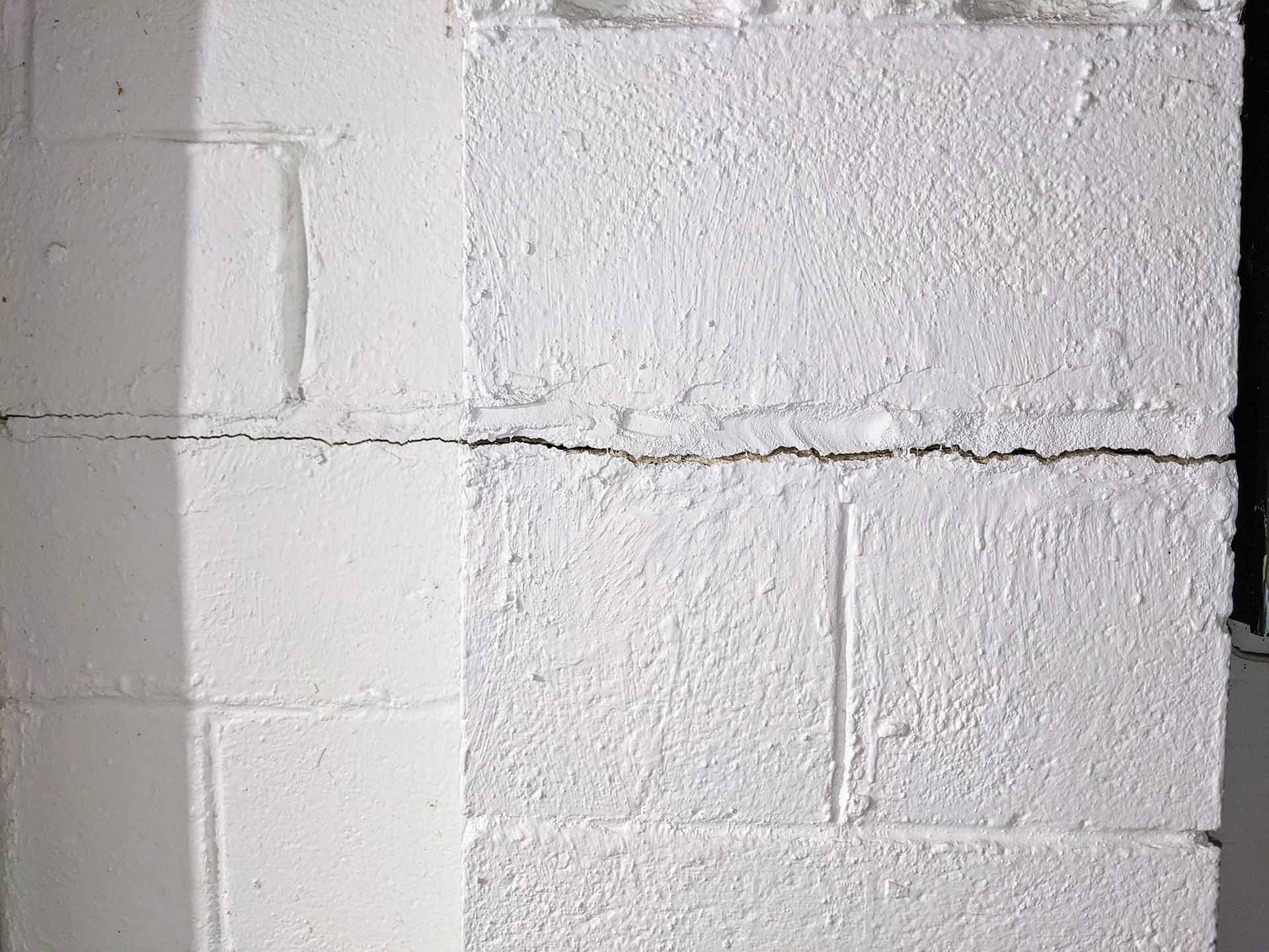 A horizontal crack runs through the middle of a painted white cinder block wall.