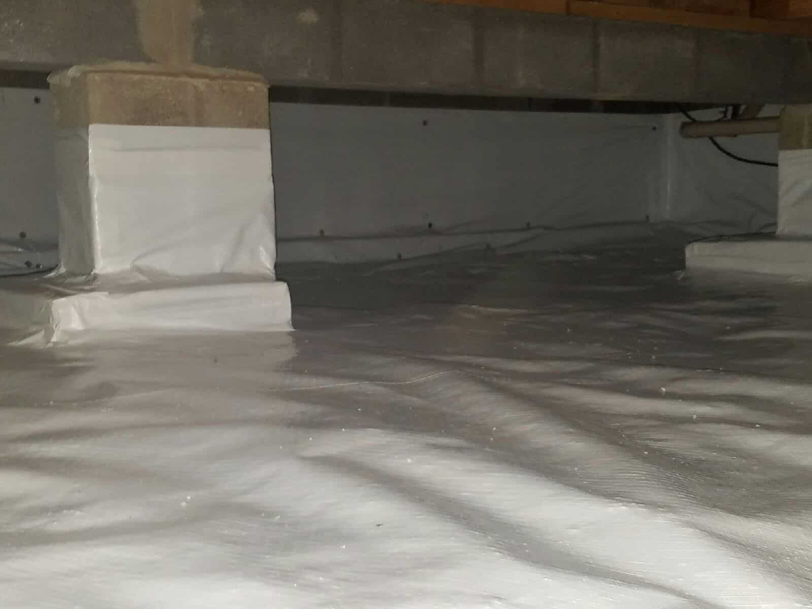 A crawl space with concrete support pillars, covered in a clean, white vapor barrier liner for moisture control.
