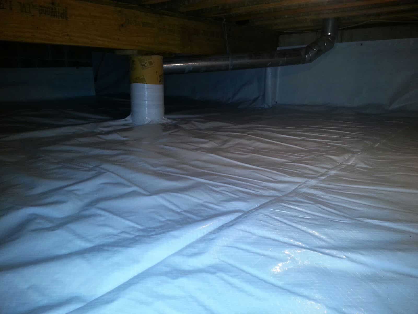 A crawl space with a plastic vapor barrier covering the floor and a pipe running along the ceiling.