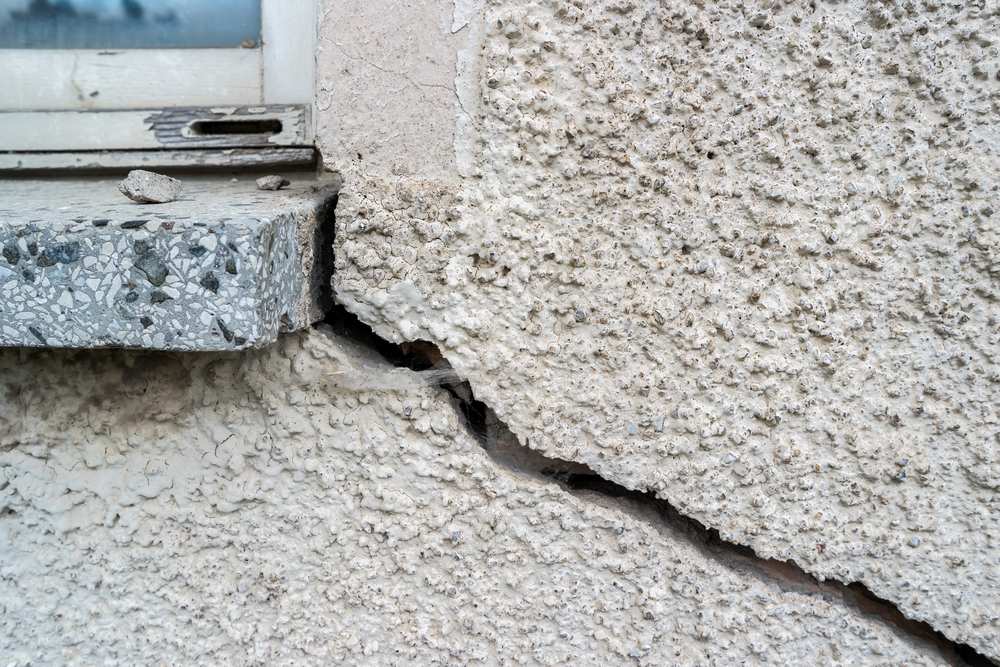 A large crack runs through a rough-textured exterior wall beneath a chipped windowsill.
